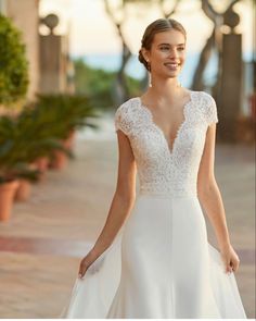 a woman in a white wedding dress standing on a brick walkway with palm trees behind her