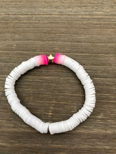 a white bracelet with pink and gold beads on top of a wooden table next to a cell phone