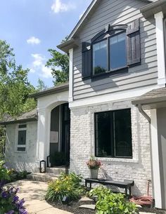 a white brick house with black shutters and flowers in the front yard, on a sunny day