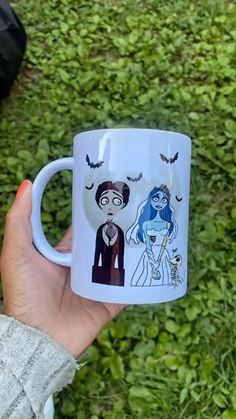 a person holding a coffee mug with cartoon characters on it in front of some grass