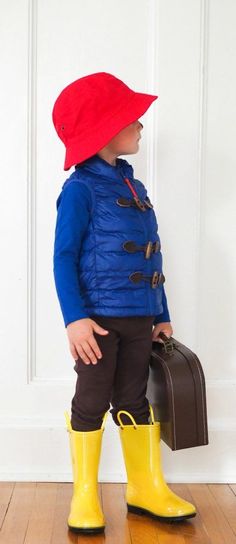 a little boy wearing yellow rubber boots and a blue jacket with a red hat on his head