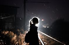 a woman standing on train tracks at night with her back turned to the camera,