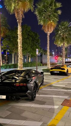 two black sports cars parked on the side of the road at night with palm trees in the background