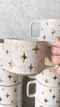 a hand holding a coffee cup with gold stars on it and five cups stacked in the background