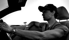 a man sitting in the driver's seat of a car with his hand on the steering wheel