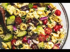 a bowl full of pasta salad with tomatoes, cucumbers and other vegetables in it