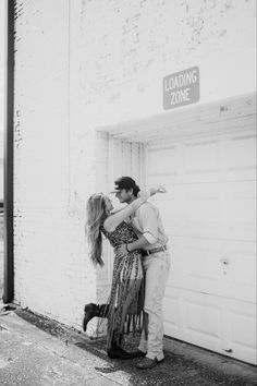 a man and woman kissing in front of a garage door with loading zone sign above them