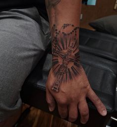 a man with a cross tattoo on his arm and hand is sitting in a chair