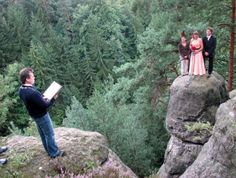 three people standing on top of large rocks in the middle of a forest with trees