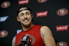 a man in a red jersey is smiling at the camera with a microphone behind him