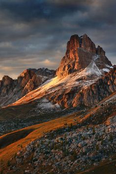 the mountains are covered in snow and rock as the sun sets over them on a cloudy day