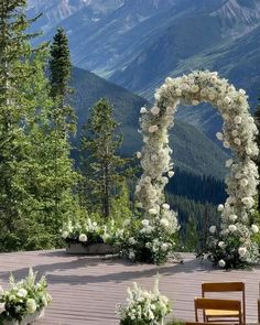 an outdoor ceremony set up with white flowers and greenery in front of the mountains