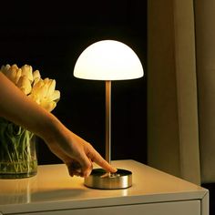 a person touching the light on a table with flowers in a vase next to it