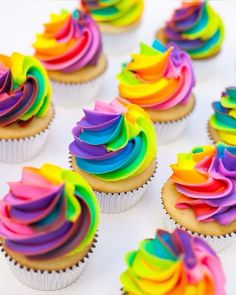 cupcakes with rainbow frosting are arranged on a table