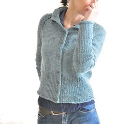 a woman is wearing a blue sweater and holding her hand to her mouth while standing in front of a white wall