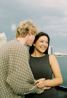 two people standing next to each other near the water