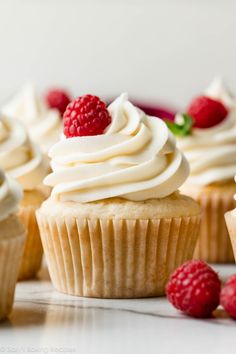 several cupcakes with white frosting and raspberries on the top one