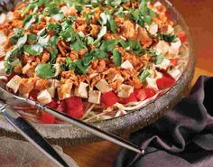 a large bowl filled with lots of food on top of a wooden table next to utensils