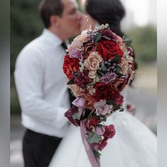 a bride and groom kissing in front of the camera with red flowers on their bouquet