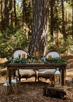 a wooden table with candles and greenery on it in the middle of a forest