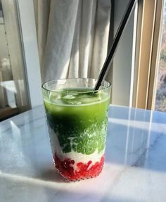 a green and red drink sitting on top of a white table next to a window