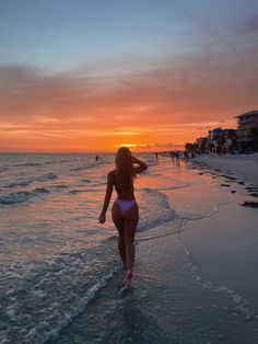 a woman walking on the beach at sunset with her back to the camera as she walks into the water