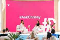 two women sitting on white chairs in front of a pink backdrop with the hash logo