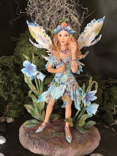 a fairy figurine sitting on top of a rock next to flowers and grass