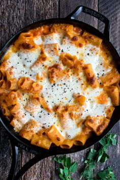 a skillet filled with pasta and cheese on top of a wooden table next to parsley