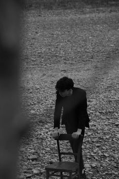 a man standing on top of a wooden chair in the middle of a gravel field