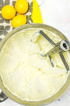 a metal bowl filled with white frosting next to lemons and a pair of scissors