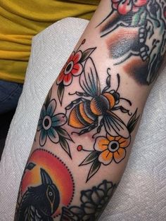 a woman's arm with tattoos on it and flowers in the background, including a bee