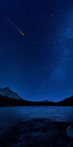 the night sky is lit up with stars and an airplane in the distance above water