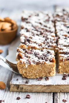 a wooden cutting board topped with granola bars next to a bowl of almonds