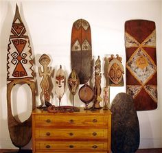 an assortment of african art on display in a room with white walls and wooden furniture