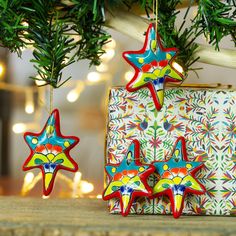 three wooden stars hanging from a christmas tree next to a present box and pine branches