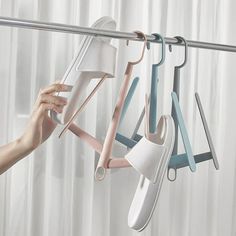 a person is holding up several pairs of shoes hanging from a rack in front of a curtain