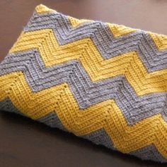 a close up of a knitted yellow and gray blanket on a table with a cell phone