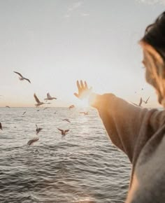 a woman is looking at birds flying over the water