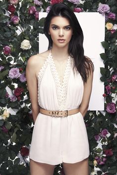 a beautiful young woman standing in front of a flower covered wall wearing a white dress