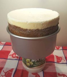 a cake sitting on top of a metal pan covered in frosting next to a red and white checkered table cloth