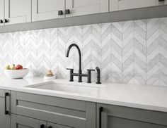 a white kitchen with marble herringbone backsplash and black faucet handles