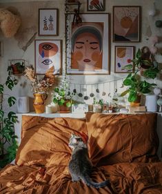 a cat sitting on top of a bed covered in an orange comforter next to potted plants