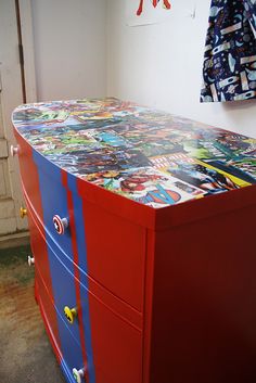 a red, blue and white dresser with comic print on it's drawers in a room