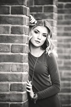 a woman leaning against a brick wall