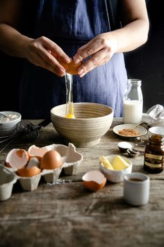 a person is mixing eggs in a bowl on a wooden table with other ingredients around it