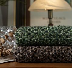 two folded blankets sitting on top of a wooden table next to a lamp and glass vase