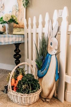 a basket filled with vegetables next to a white picket fence and a rabbit figurine