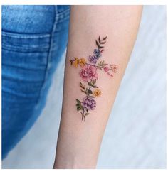 a woman's arm with flowers on it and a cross tattooed on the wrist