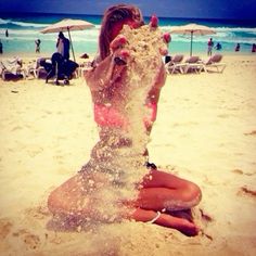 a woman is sitting on the beach and throwing sand into the air with her hands